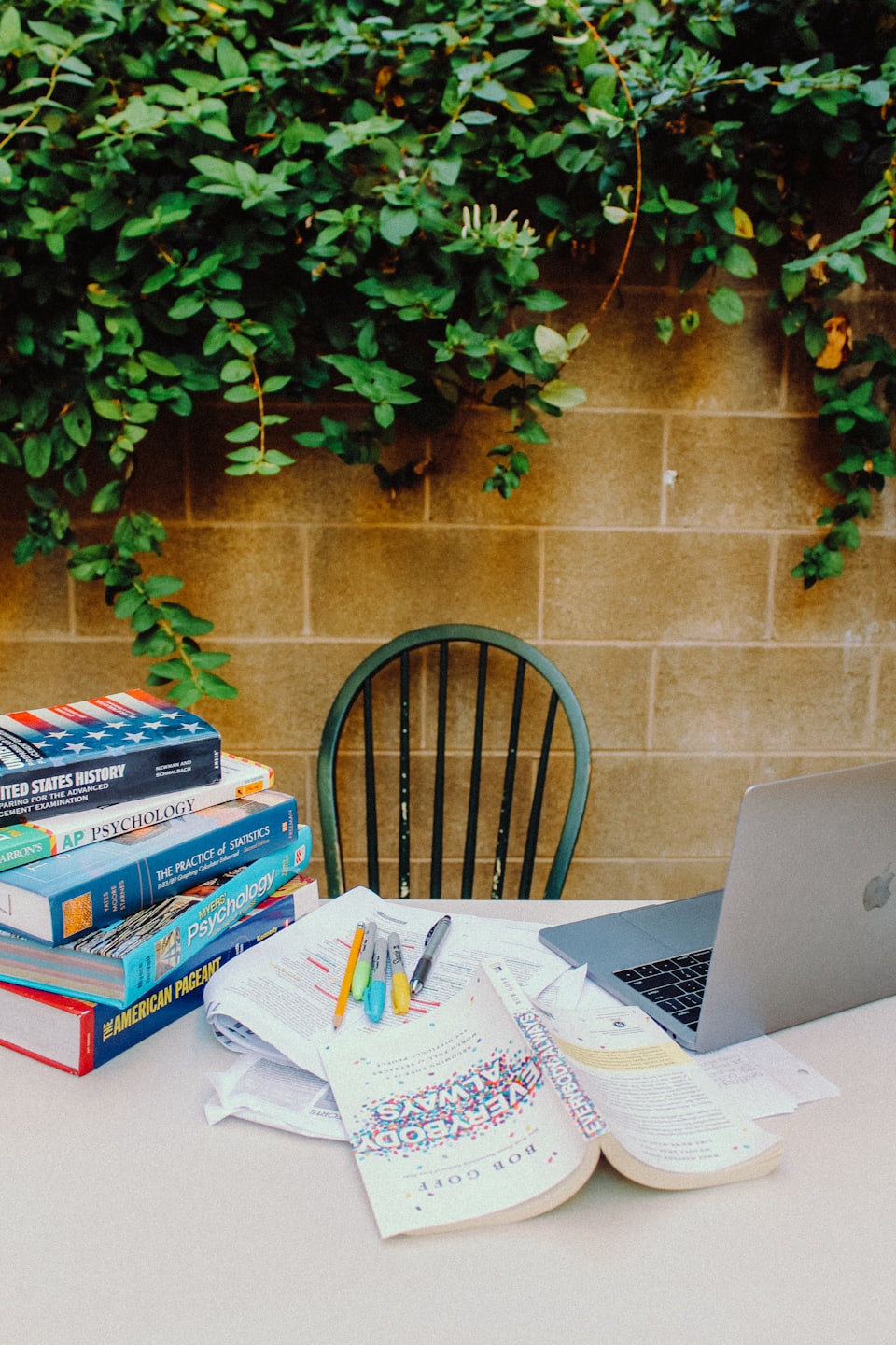 Open textbook and stack of books on a table outdoors.